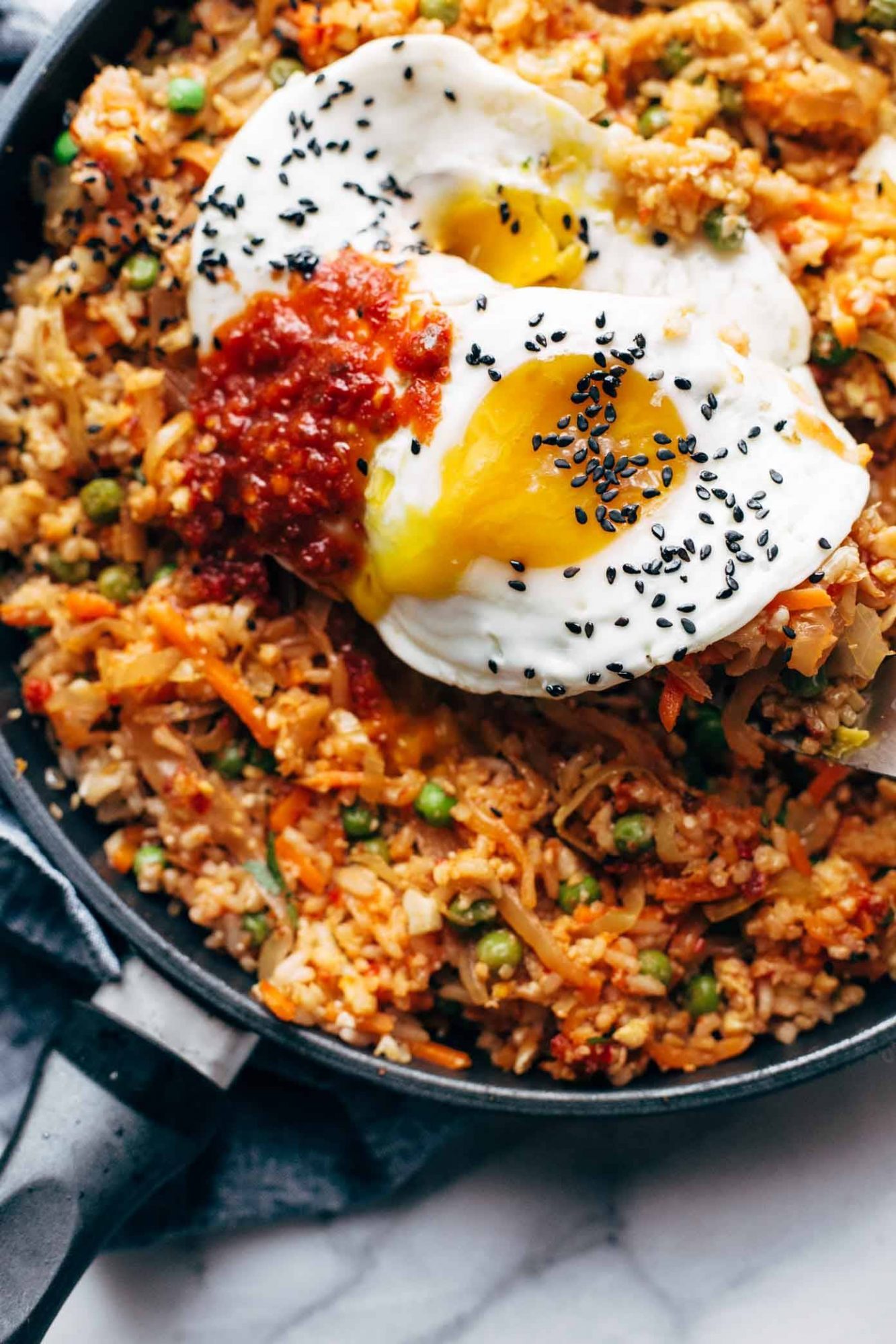 A bowl of kimchi fried rice topped with a sunny-side-up egg, garnished with green onions and sesame seeds.