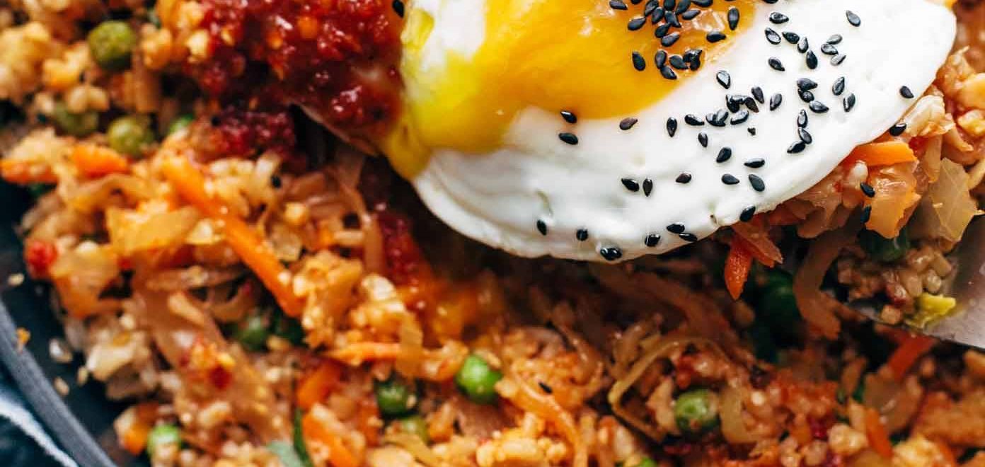 A bowl of kimchi fried rice topped with a sunny-side-up egg, garnished with green onions and sesame seeds.