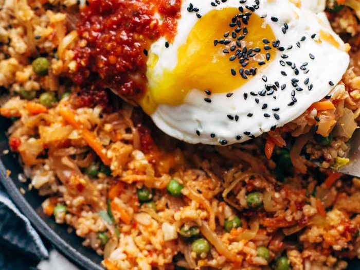 A bowl of kimchi fried rice topped with a sunny-side-up egg, garnished with green onions and sesame seeds.